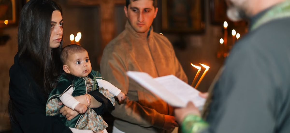 A family participates in a traditional religious ceremony with candlelight indoors.
