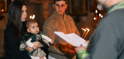 A family participates in a traditional religious ceremony with candlelight indoors.