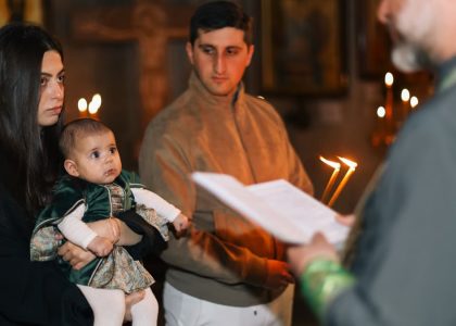A family participates in a traditional religious ceremony with candlelight indoors.